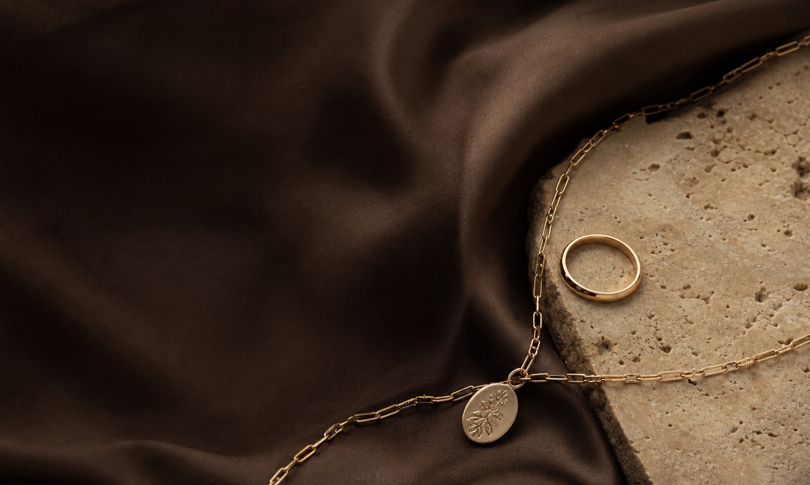 Fine gold chain and band forming a continuous line across espresso silk and warm stone